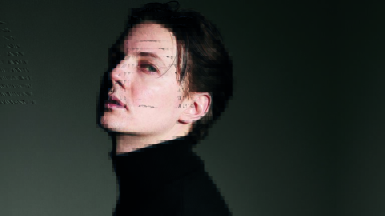 Portret van een persoon met kort donker haar tegen een donkere achtergrond.