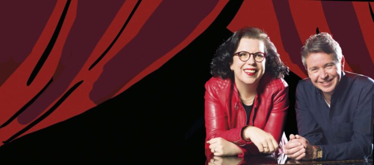 Glimlachende vrouw met donker haar en brillen, gekleed in een rode jas tegen een rood grafisch patroon.