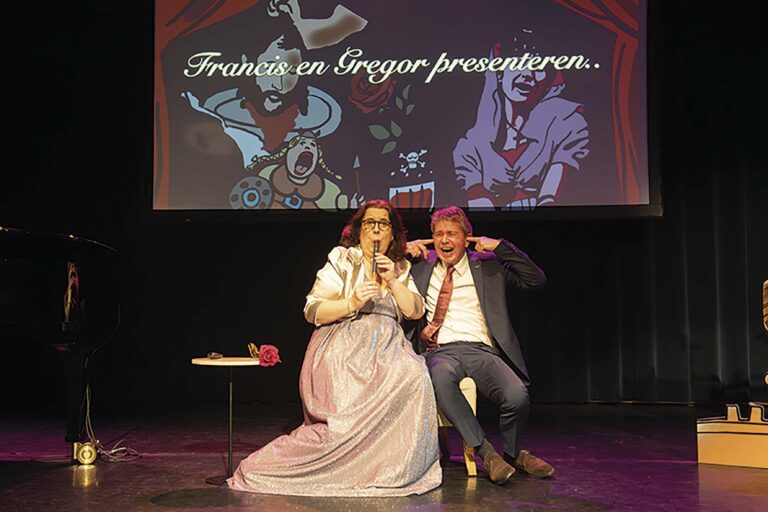 Een vrouw in een witte bruidsjurk en een man in een pak poseren samen op een theaterpodium.
