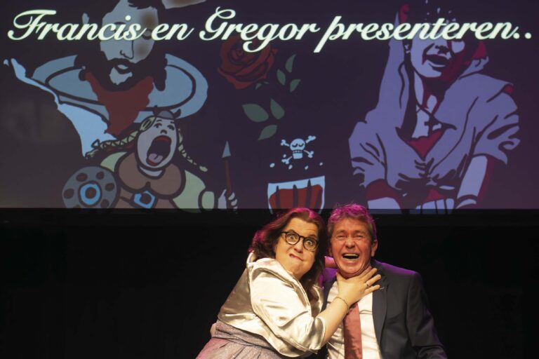 Twee mensen poseren samen op een podium voor een kleurrijke projectorachtergrond.