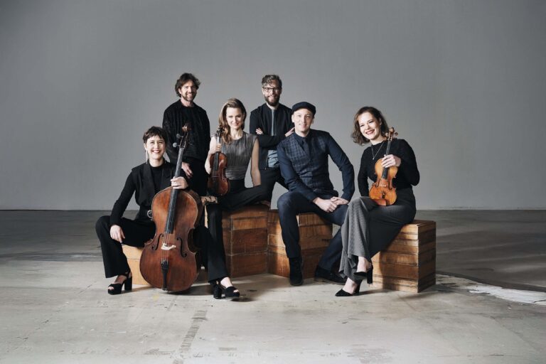 Een groep strijkers poseert samen in een studio, met cello’s en violen.