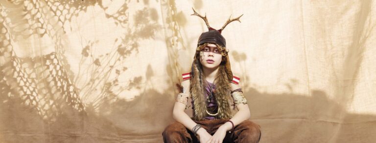 Een persoon draagt een hoofddeksel met rendierantlers en bontkleding met kralen.