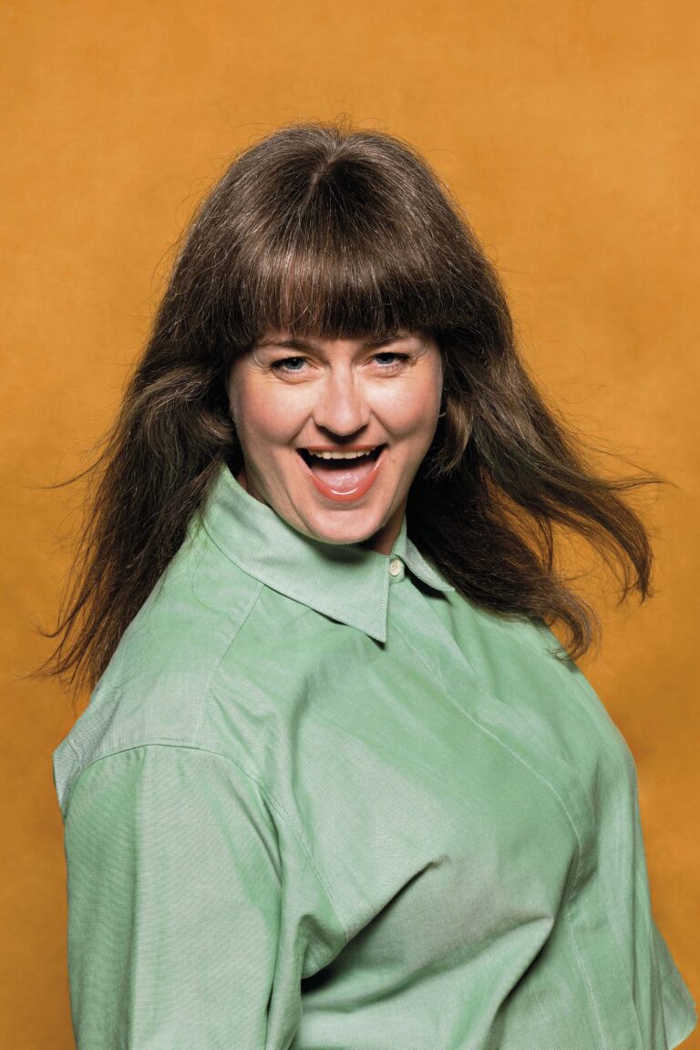 Een vrouw met een groene blouse glimlacht tegen een oranje achtergrond.