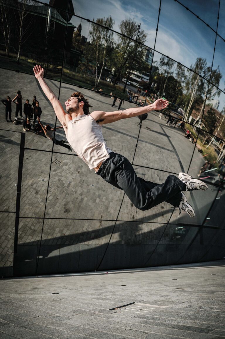 Een skateboarder maakt een sprong in de lucht tijdens een skateboardtrick op een skatebaan, met toeschouwers op de achtergrond.
