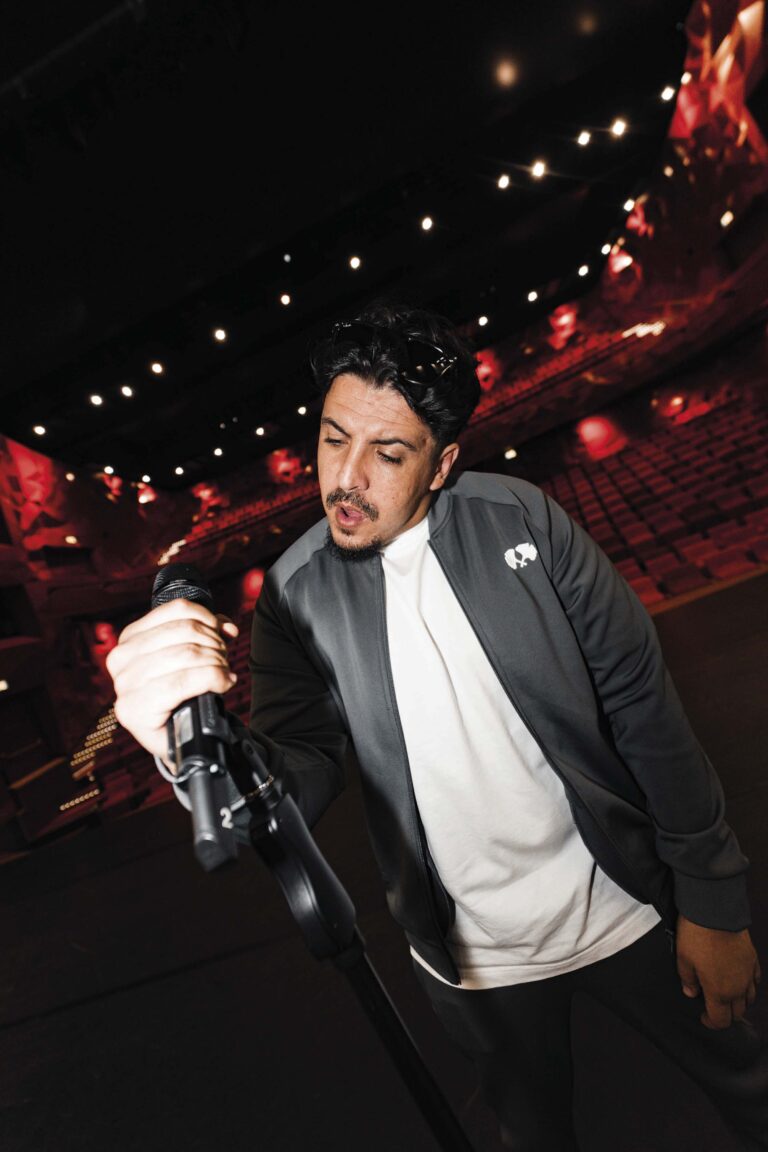 Een man in een donker pak op een podium houdt een microfoon vast tijdens een optreden.