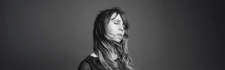 Zwart-wit portret van een vrouw met lang haar, met haar gezicht deels bedekt en haar blik naar beneden gericht.