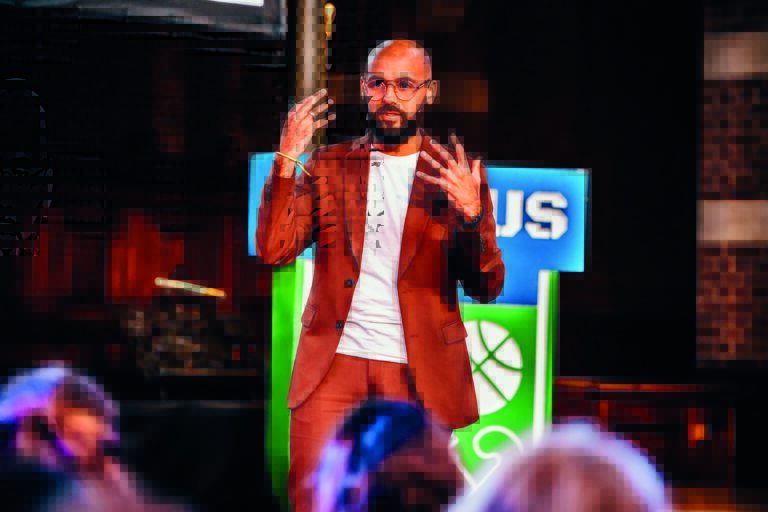 Een man in een rode jas staat op een podium tijdens een optreden.