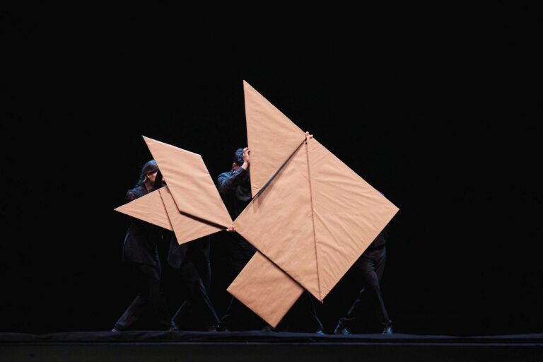 Meerdere zandkleurige gevouwen origami-vormen tegen een zwarte achtergrond.