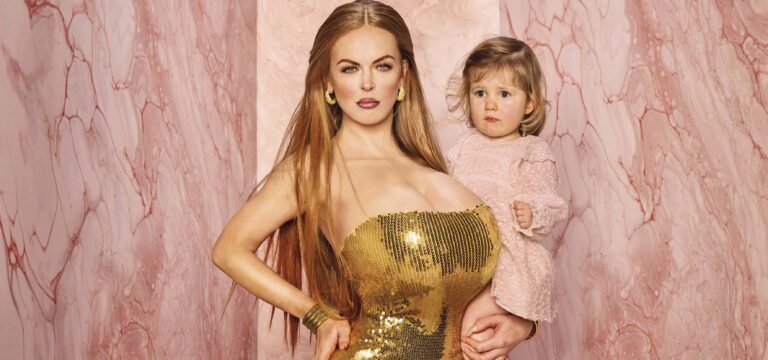 Een vrouw in een gouden jurk poseert met een klein kind naast zich voor een roze achtergrond.