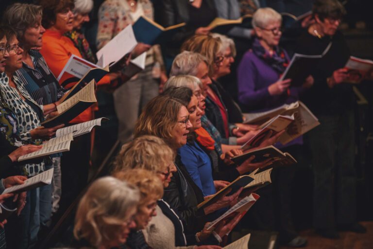 Een groep vrouwen zingt samen en leest uit muziekboeken tijdens een kooroptreden.