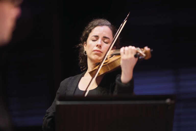 Een muzikante speelt intens op haar viool tijdens een optreden.