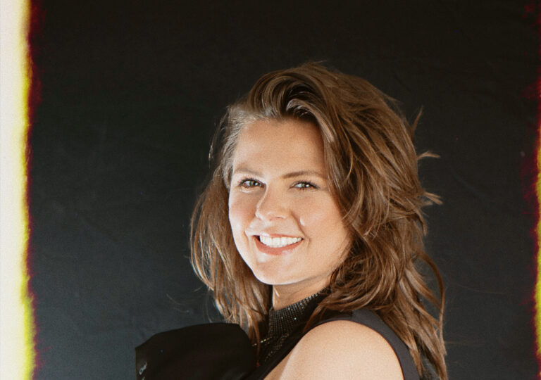 Portret van een glimlachende vrouw met bruin haar tegen een donkere achtergrond.