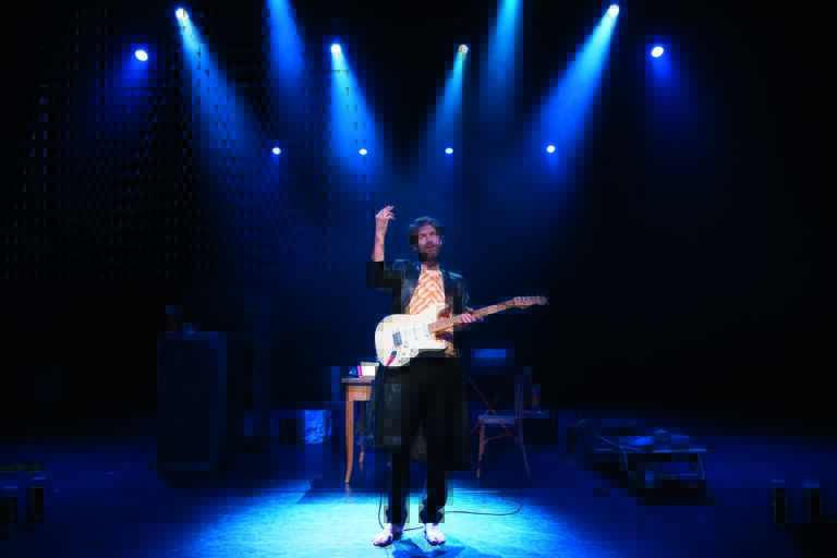 Een muzikant met een gitaar staat in de schijnwerpers op een podium.