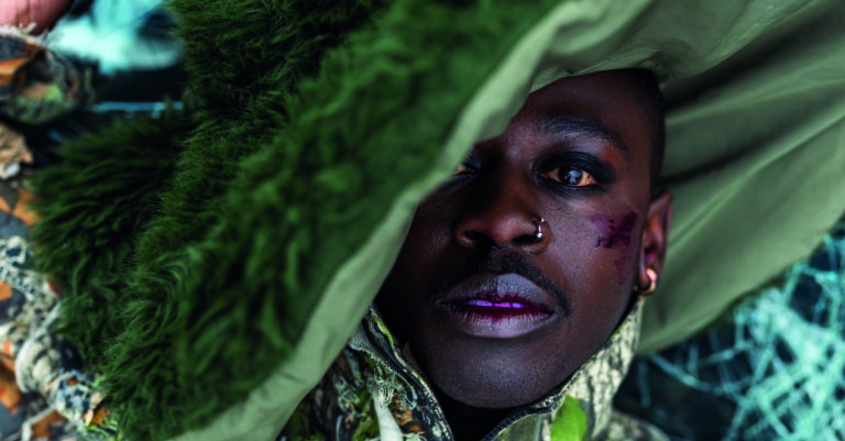 Een close-up van een persoon wiens gezicht grotendeels verborgen is onder een groene doek, met opvallende make-up op de lippen en rondom de ogen.