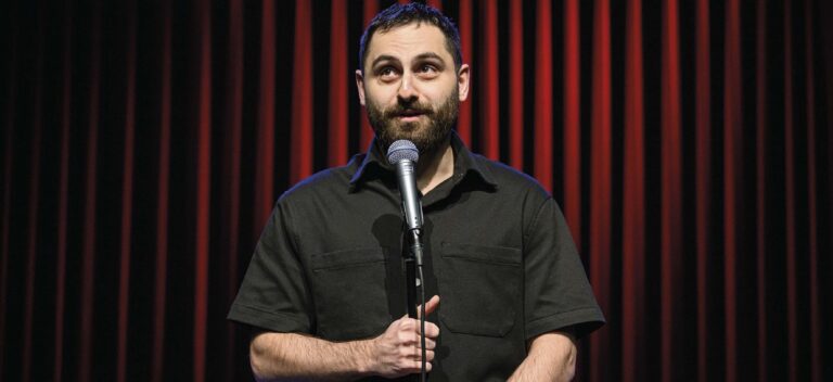 Een man met een microfoon op het podium voor rode gordijnen.