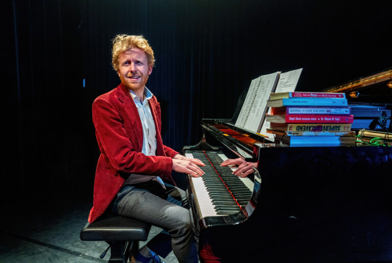 Een muzikant speelt enthousiast piano met boeken en bladmuziek op het instrument.