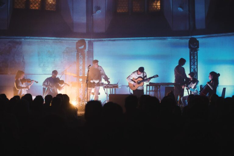 Een band speelt live muziek op een podium, omringd door een enthousiast publiek en kleurrijke verlichting.