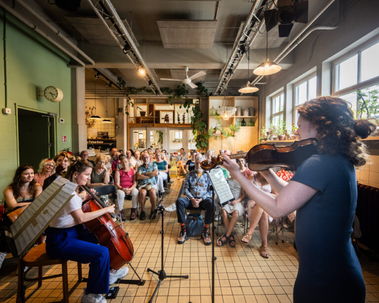 Een groep mensen luistert naar een live muziekoptreden in een gezellige, goed verlichte ruimte.