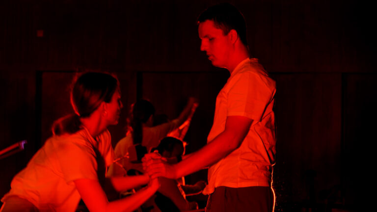 Twee personen voeren een dansuitvoering uit in een omgeving met rode verlichting.