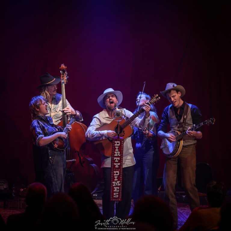 Een groep muzikanten speelt op het podium met verschillende instrumenten, onder sfeervolle verlichting.