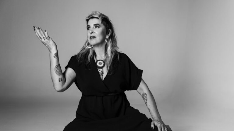 Zwart-witportret van een vrouw in een jurk, zittend en met een hand omhoog.