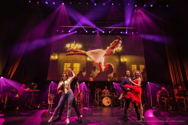 Een levendige podiumperformance met dansers en muzikanten, verlicht door kleurrijke lichten en een grote achtergrondprojectie.