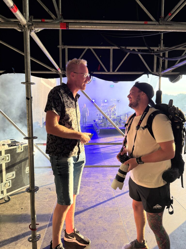 Twee mannen staan in gesprek op een podium, met een rookachtige achtergrond en apparatuur om hen heen.