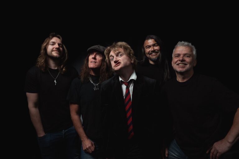 Een rockband met vijf leden poseert samen tegen een zwarte achtergrond.