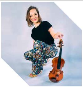 Een vrouw in een zwarte T-shirt en kleurrijke broek knielt naast een viool op de grond.