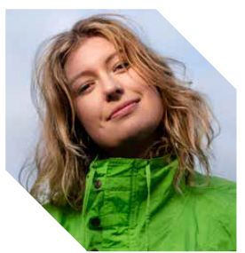 Een vrouw met een sportieve uitstraling draagt een groene jas en kijkt recht in de camera.