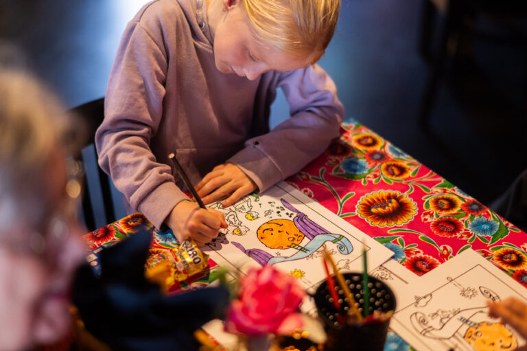 Een meisje kleurt geconcentreerd op een kleurplaat aan een kleurrijke tafel.