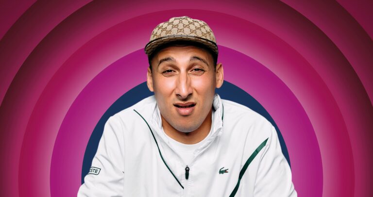 Man met een neutrale uitdrukking, gekleed in een witte jas en een herkenbare hoed, tegen een paarse, golvende achtergrond.