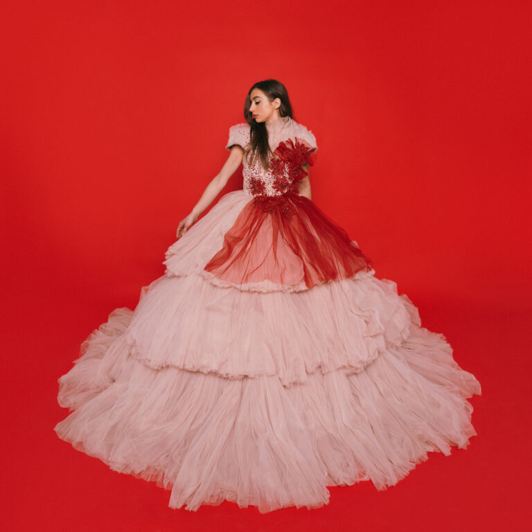 Een vrouw in een extravagante rozenoverhemd met een volle, gelaagde rok in zachte tinten van roze en rood, zaliger tegen een helderrode achtergrond.
