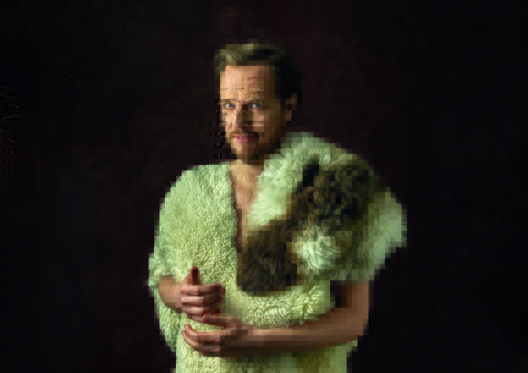 Een persoon in een groene, vachtachtige deken poseert tegen een donkere achtergrond.