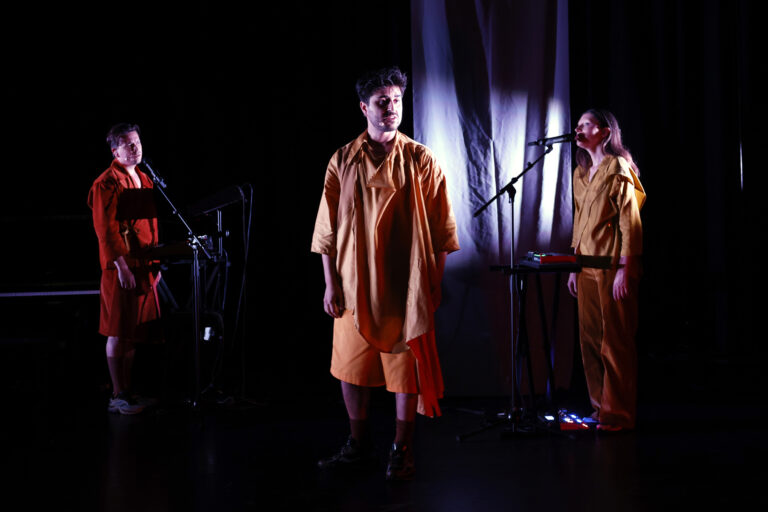 3 mensen zingend op donker toneel