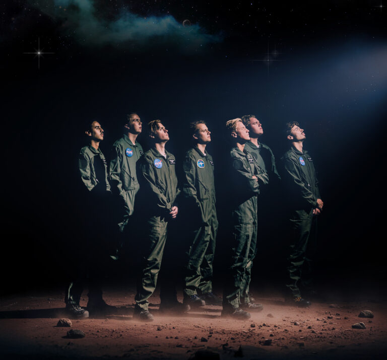 Zeven mannen in groene NASA pakken kijkend naar rechts naar het heelal.