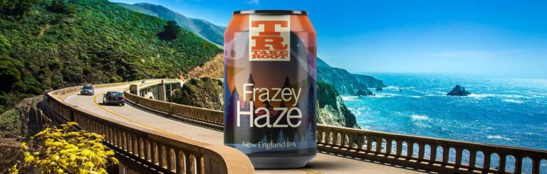Een blik bier met het label “Frazey Haze” op een houten railing, met bergen en een heldere blauwe lucht op de achtergrond.