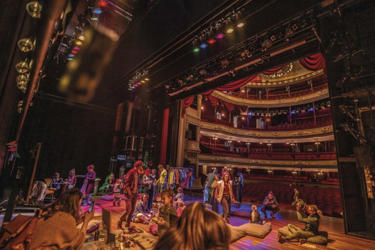 Theaterpodium met een groep performers tijdens een voorstelling, met publiek in de zaal.