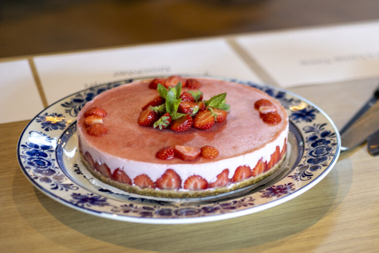 Roze glazuurtaart met aardbeien langs de rand, geplaatst op een blauw-wit bord.