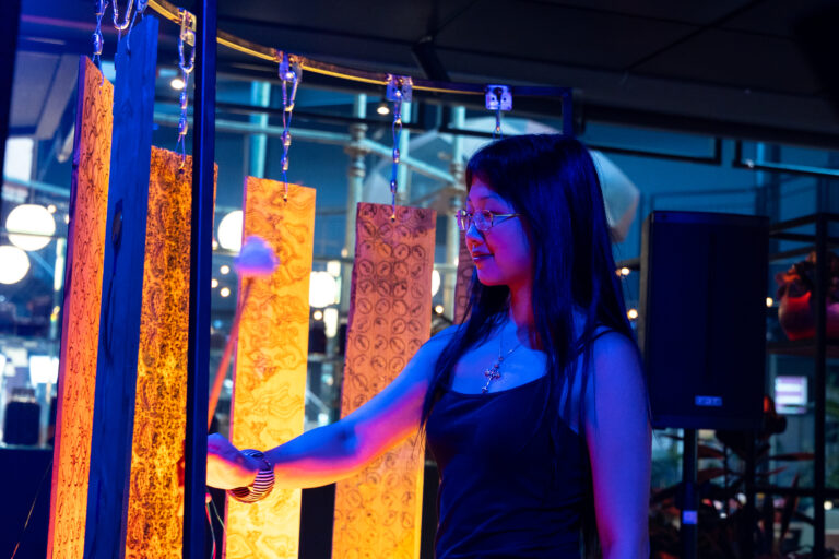 Een vrouw in een donker jurkje staat voor fel oranje lichtpanelen in een donkere ruimte.