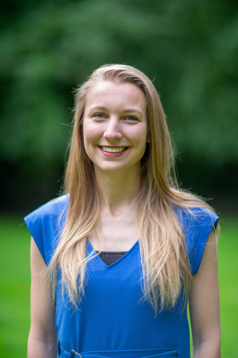 Portretfoto van Hannah Tomasini in een blauwe outfit met groene achtergrond.