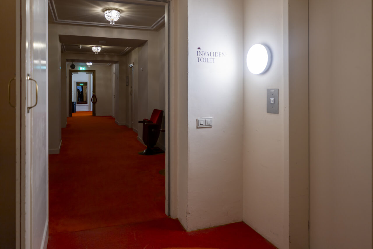 Een witte lift in een ouder gebouw met rode vloerbedekking.