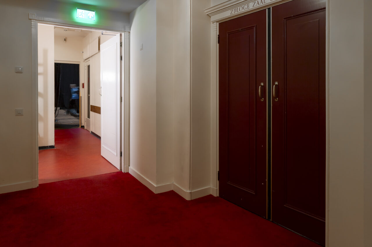 Rode dubbele klapdeur met witte muren en rode vloerbedekking in de oude Stadsschouwburg