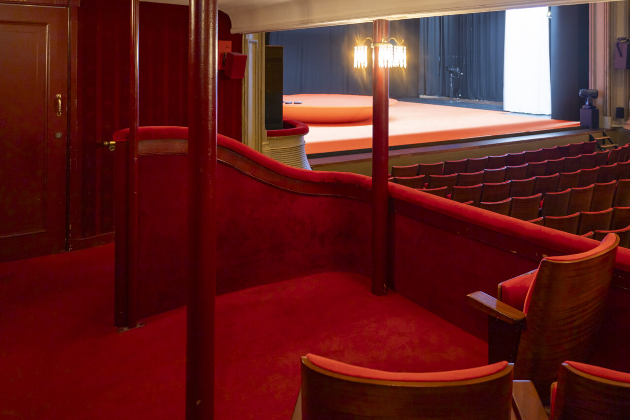 Rood beklede loge met rode palen en uitzicht op het podium.
